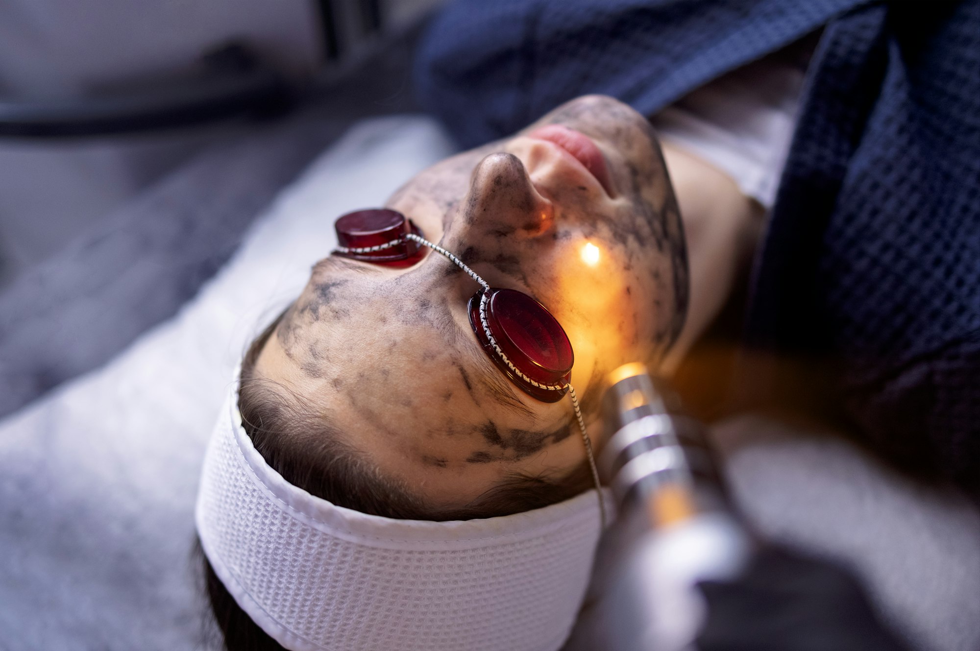 Beautician holding beauty laser near woman face covered with carbon mask