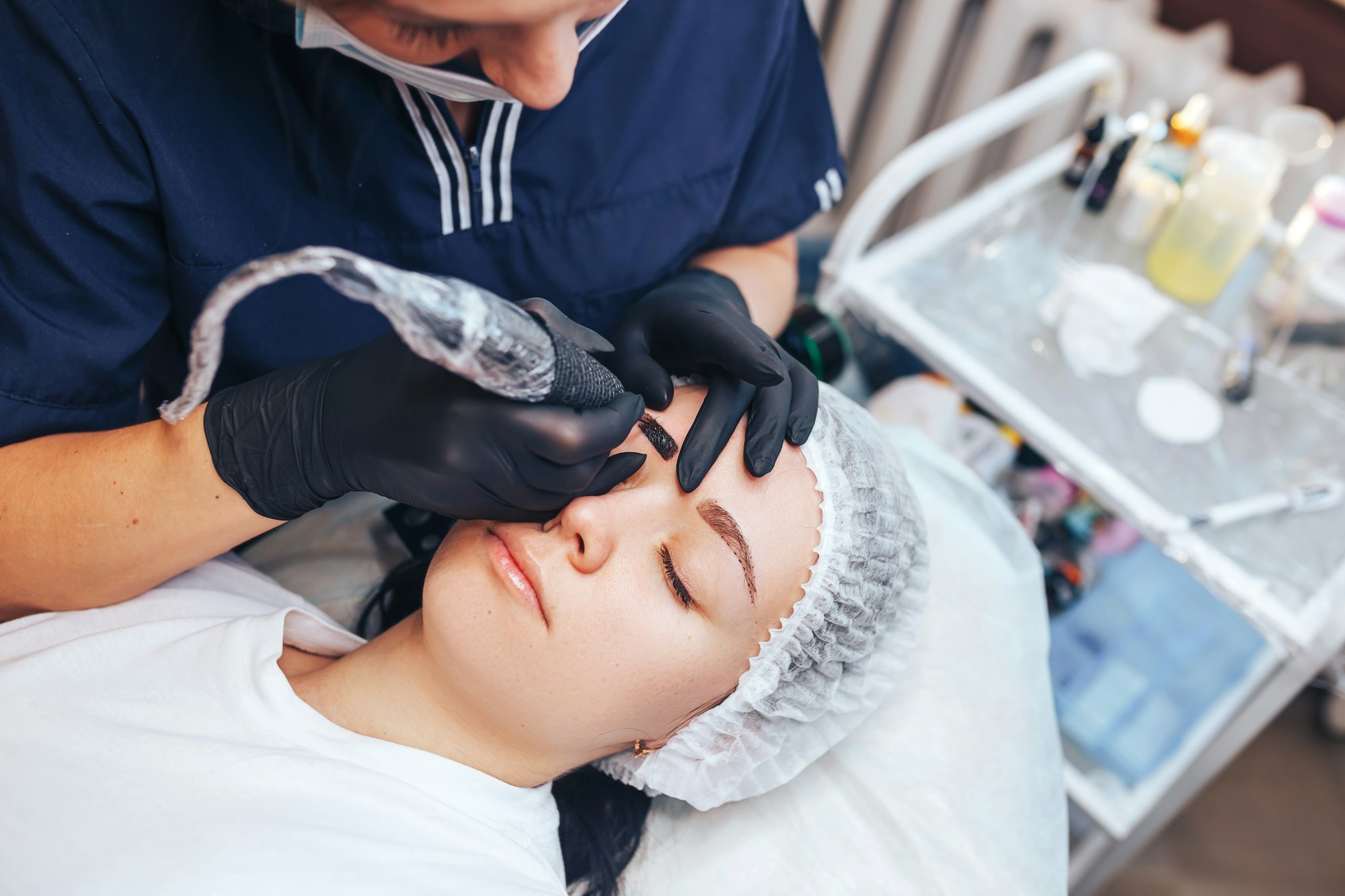 beautician making a permanent make-up procedure on eyebrows using a machine