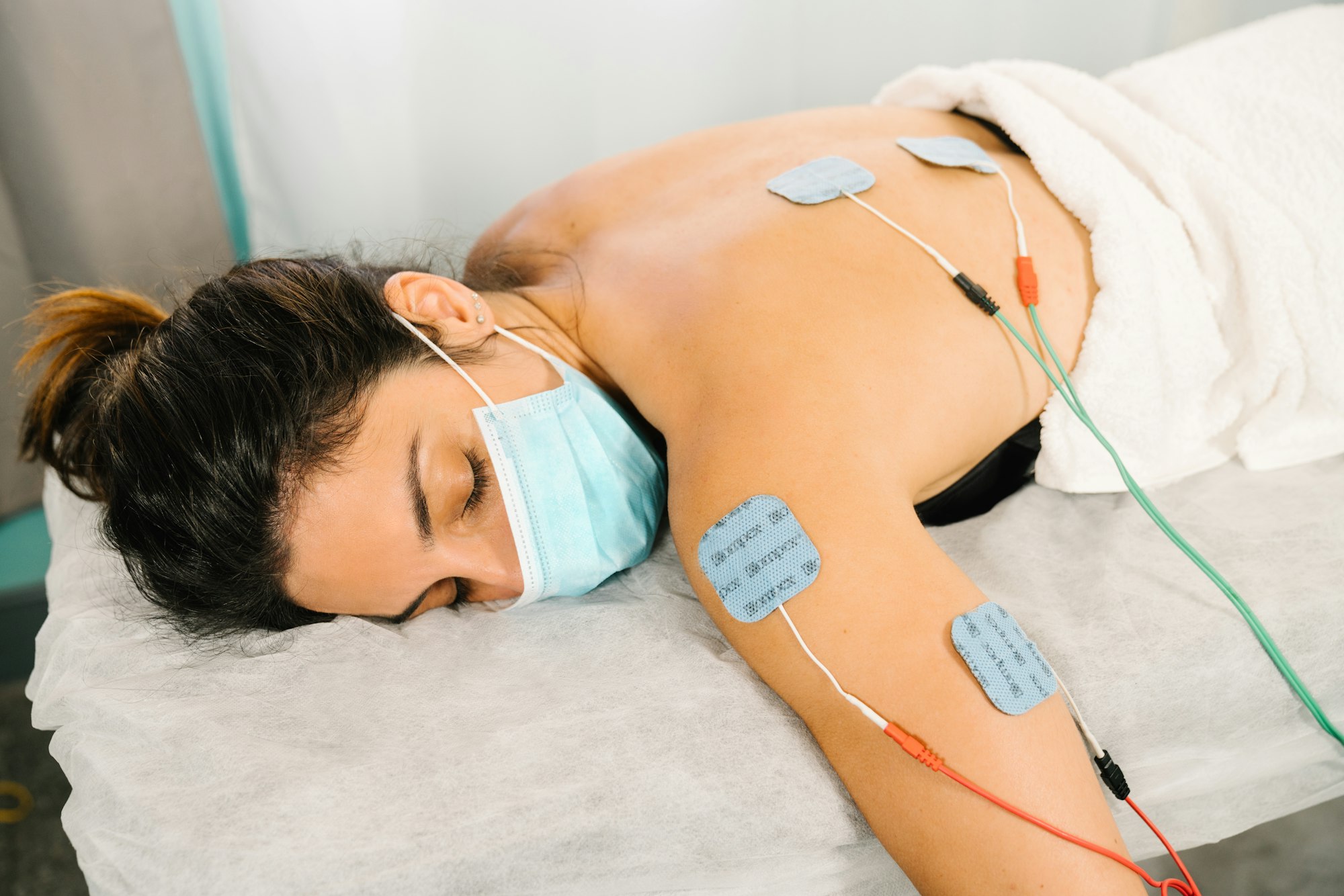 woman receiving physiotherapy treatment with electro-stimulation electrodes on her back